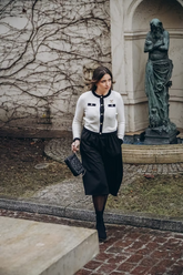 a lady wears a white cardigan with black midi skirt